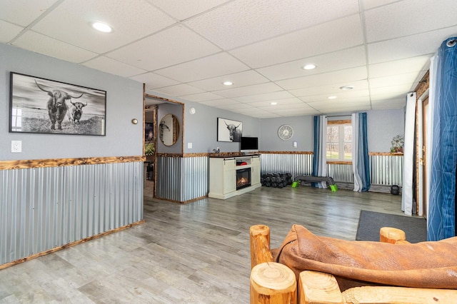 living area featuring a paneled ceiling, wood finished floors, a warm lit fireplace, and recessed lighting