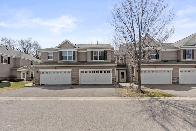 townhome / multi-family property with a garage, driveway, and stone siding
