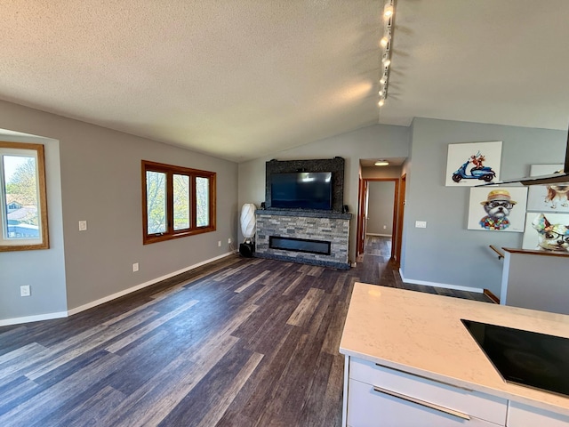 14303 Utica Ave, Savage, MN 55378 - living room featuring dark wood-type flooring, vaulted ceiling, a stone fireplace, baseboards, and rail lighting