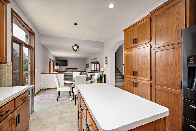 kitchen featuring a center island, brown cabinets, light countertops, and refrigerator with ice dispenser