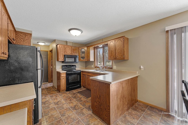 kitchen with a sink, brown cabinetry, black appliances, light countertops, and a peninsula