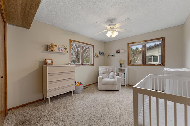 carpeted bedroom with a nursery area, baseboards, a textured ceiling, and ceiling fan