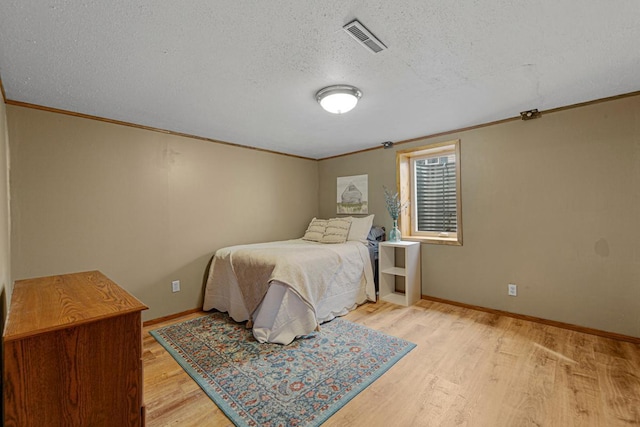 bedroom featuring light wood-style floors, visible vents, a textured ceiling, and ornamental molding