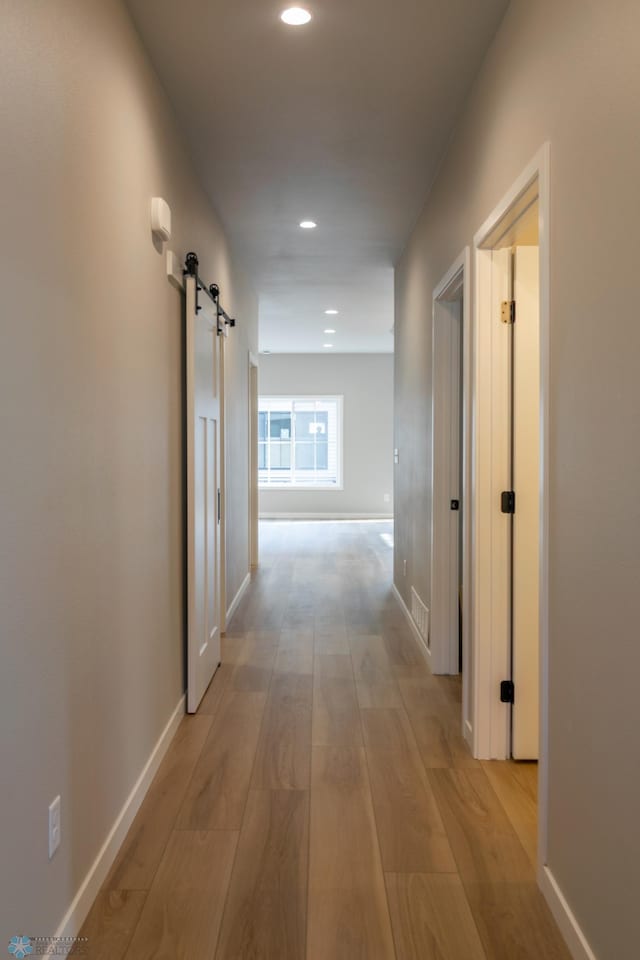 hallway with baseboards, light wood finished floors, a barn door, and recessed lighting