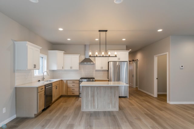 kitchen featuring light countertops, appliances with stainless steel finishes, a sink, and wall chimney range hood