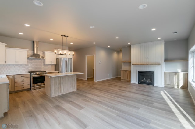 kitchen with light countertops, a center island, appliances with stainless steel finishes, and wall chimney exhaust hood