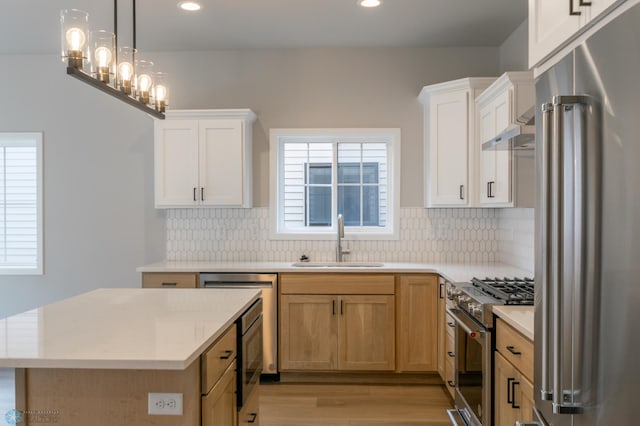 kitchen featuring light countertops, high end appliances, under cabinet range hood, light wood finished floors, and a sink
