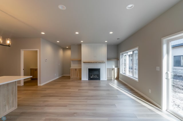 unfurnished living room featuring baseboards, an inviting chandelier, light wood-style floors, a fireplace, and recessed lighting