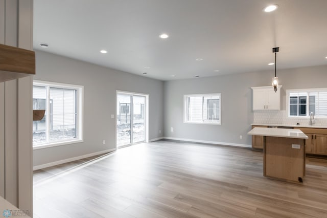 unfurnished living room with recessed lighting, a sink, light wood-type flooring, and baseboards