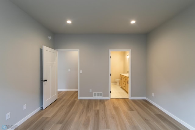 unfurnished bedroom featuring light wood finished floors, visible vents, baseboards, and ensuite bath