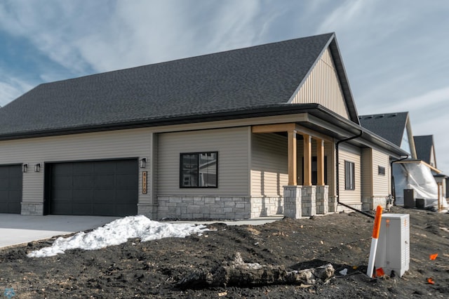 exterior space with an attached garage, concrete driveway, stone siding, and a porch
