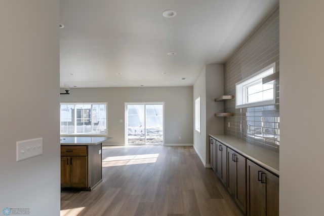kitchen with baseboards, open shelves, open floor plan, light countertops, and wood finished floors