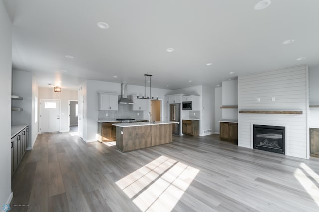 kitchen with open floor plan, light countertops, a kitchen island with sink, stainless steel appliances, and backsplash
