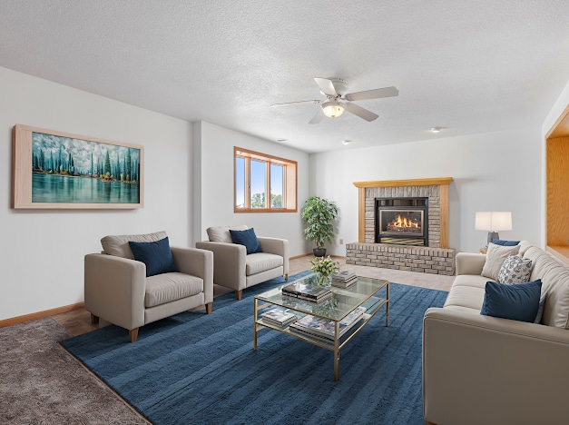 living area featuring a textured ceiling, a ceiling fan, carpet flooring, a brick fireplace, and baseboards