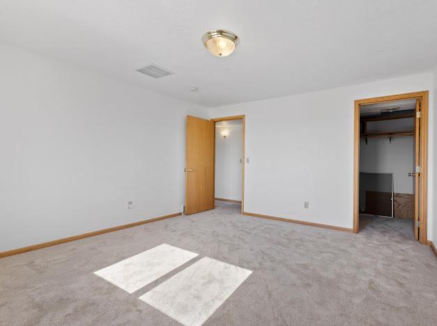 unfurnished bedroom featuring a walk in closet, carpet flooring, visible vents, and baseboards