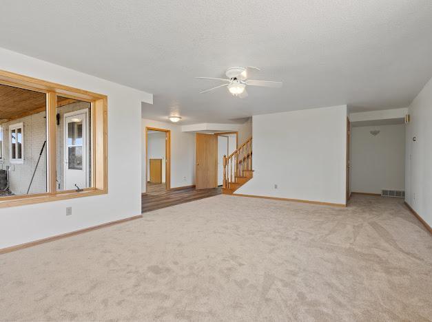 unfurnished living room featuring carpet, visible vents, baseboards, and a ceiling fan