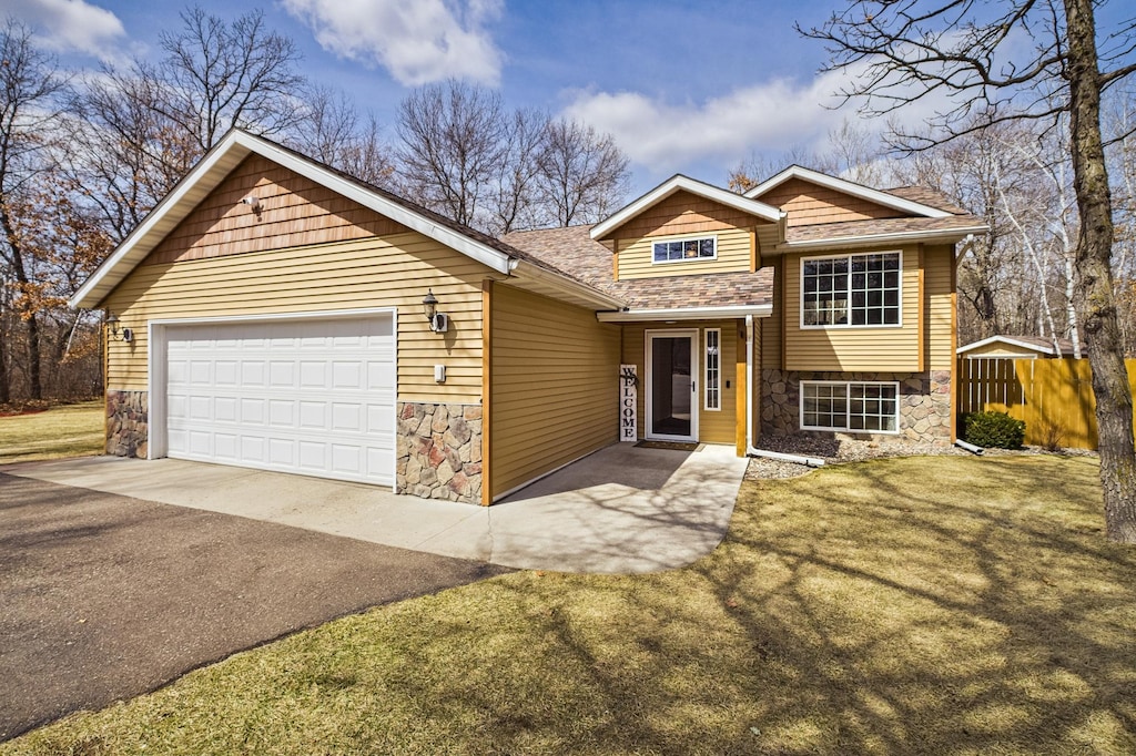 9555 Libby Ln, Brainerd, MN 56401 - split level home featuring a front lawn, aphalt driveway, stone siding, an attached garage, and fence