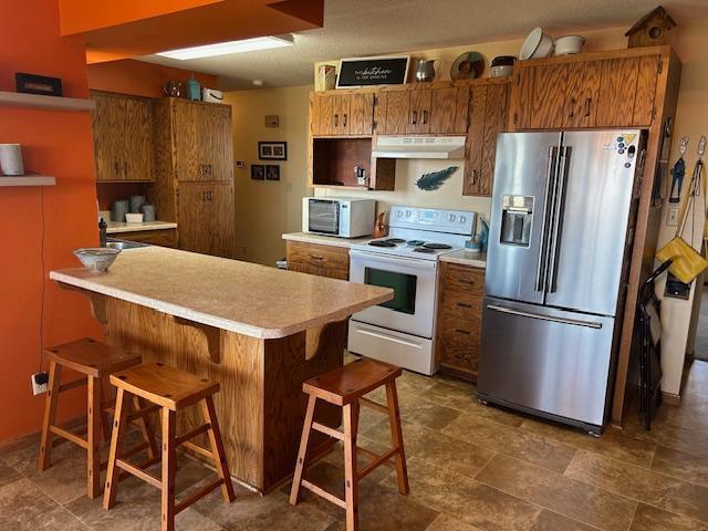 kitchen with brown cabinets, a breakfast bar, stainless steel appliances, light countertops, and under cabinet range hood