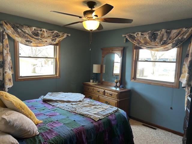 bedroom with light carpet, ceiling fan, baseboards, visible vents, and a textured ceiling