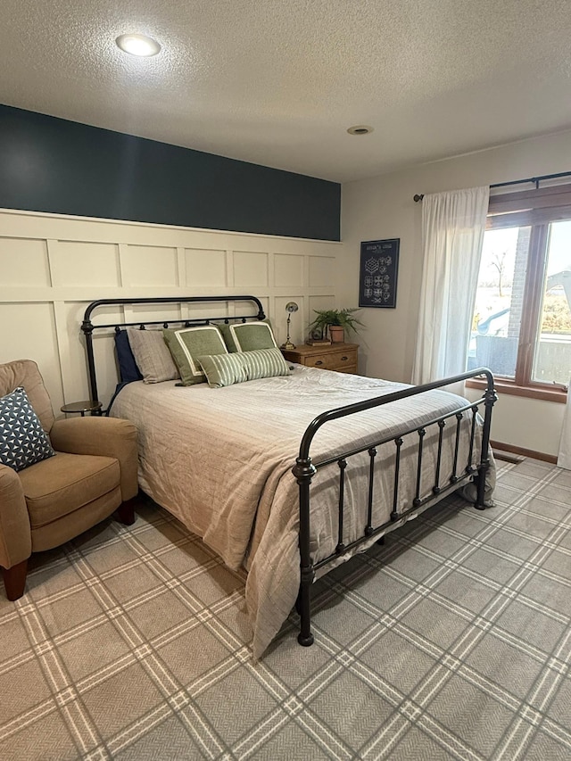 bedroom featuring a textured ceiling, a decorative wall, light colored carpet, and wainscoting