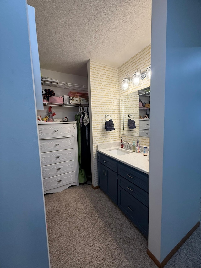 bathroom with a textured ceiling, carpet, a spacious closet, and vanity