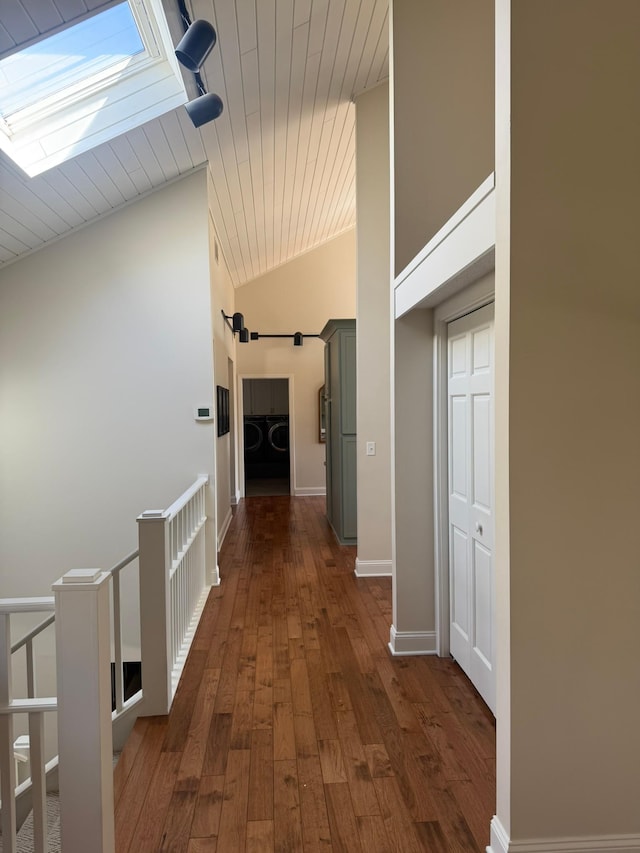 hall featuring vaulted ceiling with skylight, wooden ceiling, dark wood-style flooring, and an upstairs landing