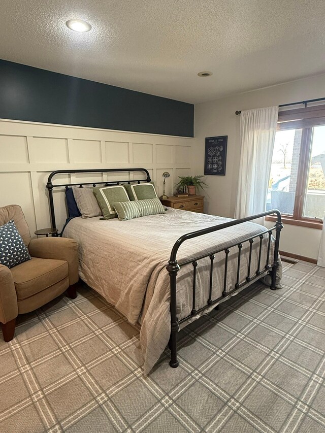 bedroom featuring a textured ceiling, a decorative wall, light colored carpet, and wainscoting