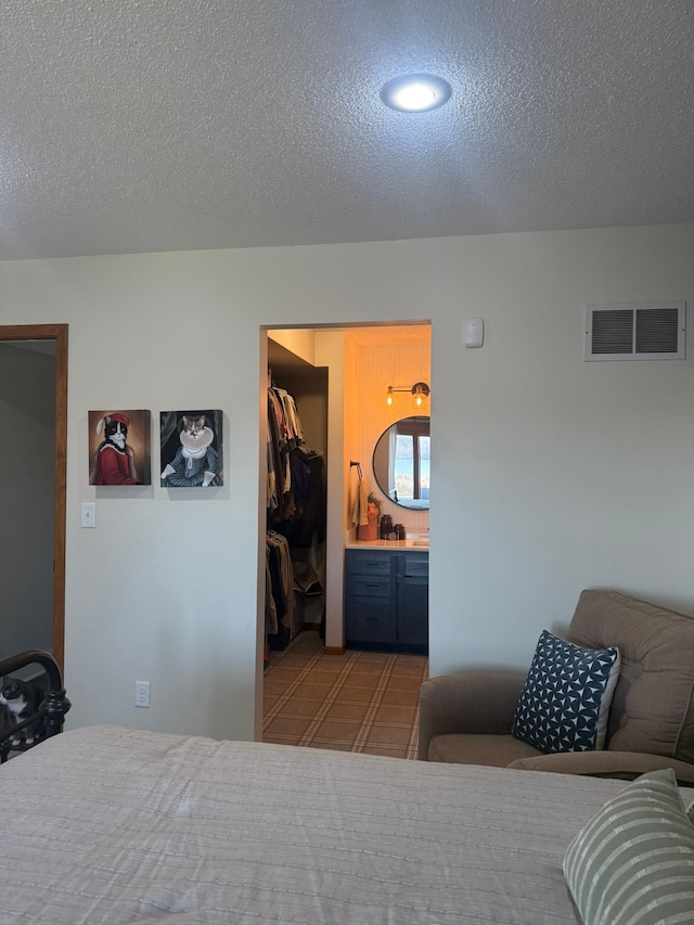 bedroom with a textured ceiling, ensuite bathroom, a spacious closet, visible vents, and recessed lighting