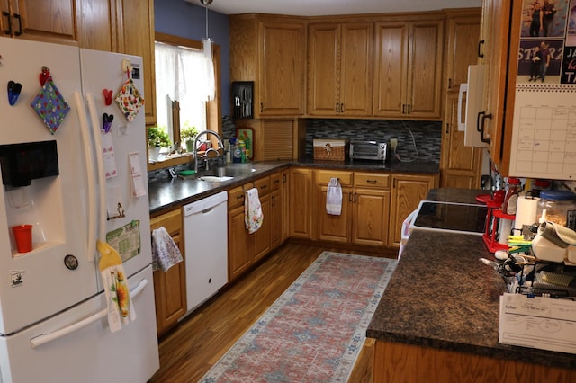 kitchen with white appliances, a sink, dark wood-style flooring, dark countertops, and backsplash