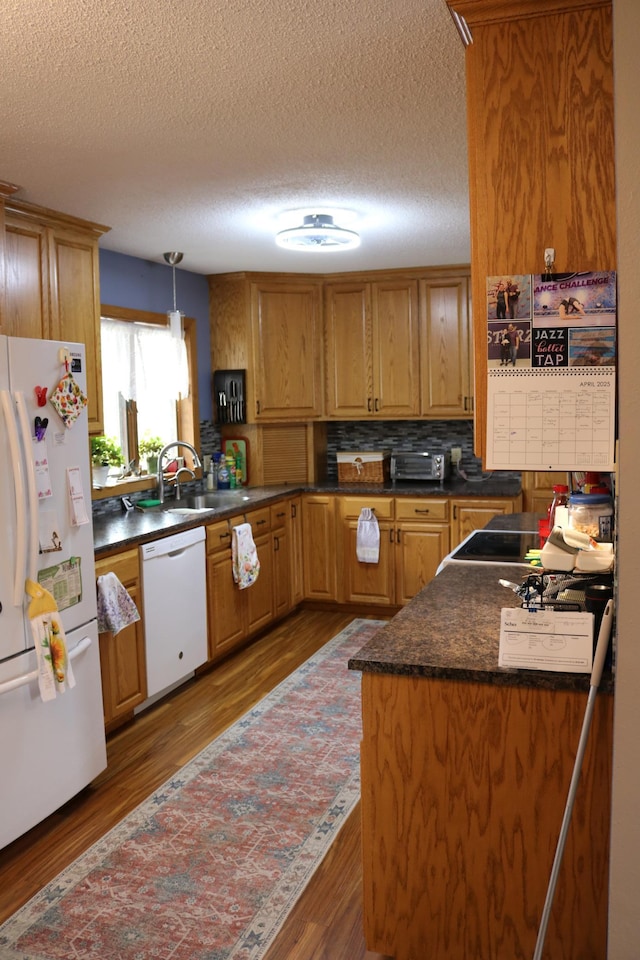 kitchen with white appliances, dark countertops, a textured ceiling, dark wood-style flooring, and a sink