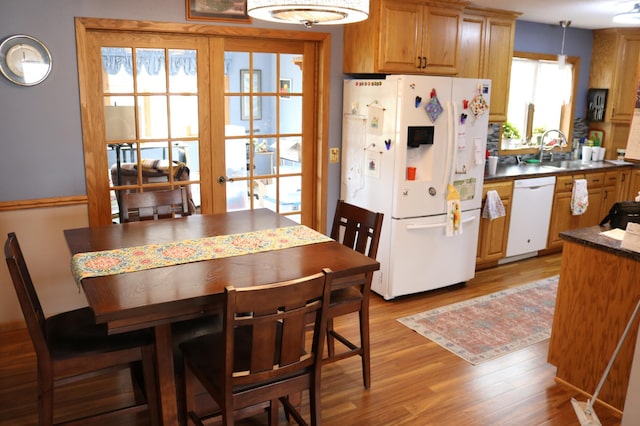 kitchen with white appliances, a sink, light wood-type flooring, dark countertops, and brown cabinetry