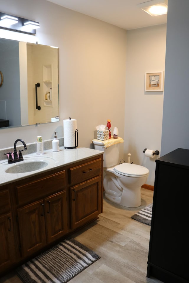 half bath with toilet, vanity, and wood finished floors