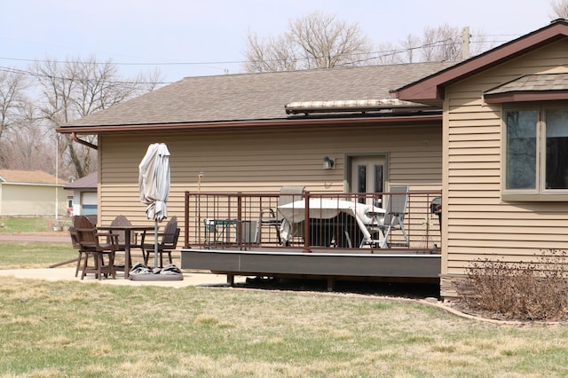 back of property featuring a wooden deck, roof with shingles, and a lawn