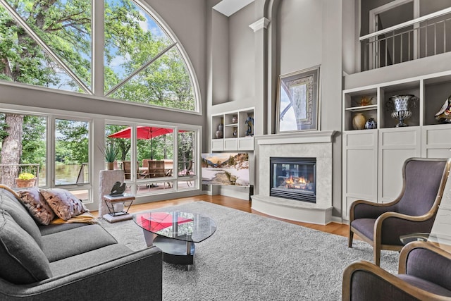 living room with a high end fireplace, built in shelves, a high ceiling, and wood finished floors
