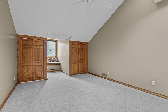 interior space with visible vents, baseboards, a ceiling fan, light colored carpet, and lofted ceiling