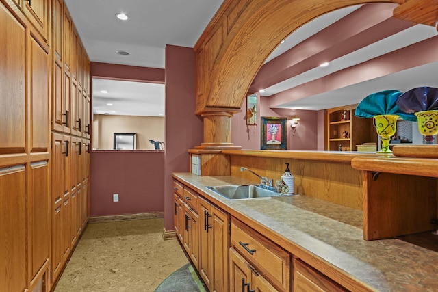 kitchen featuring baseboards, recessed lighting, light countertops, brown cabinetry, and a sink