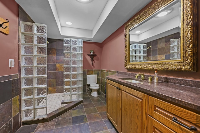 bathroom featuring tile walls, a tray ceiling, vanity, toilet, and walk in shower