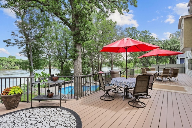 wooden terrace with outdoor dining space, a water view, and a fenced in pool