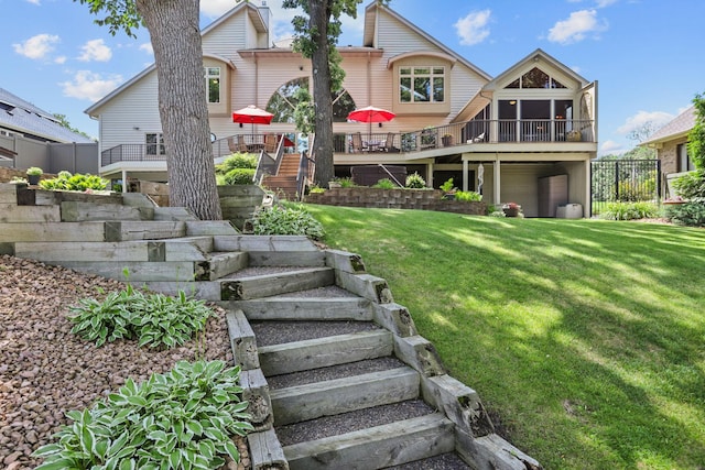 rear view of property featuring an attached garage, a wooden deck, a lawn, and stairs