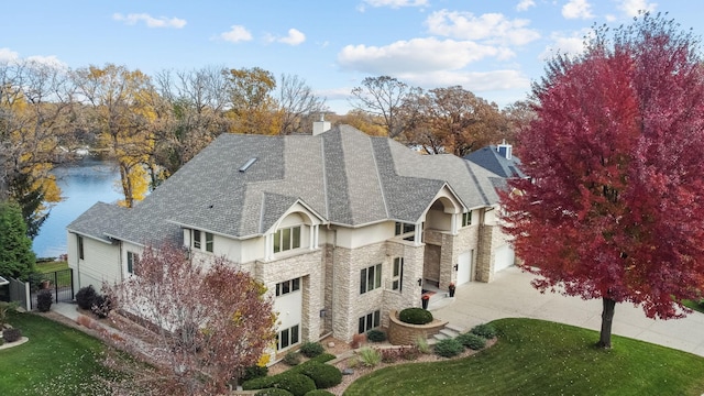 exterior space with stucco siding, a chimney, driveway, stone siding, and a water view
