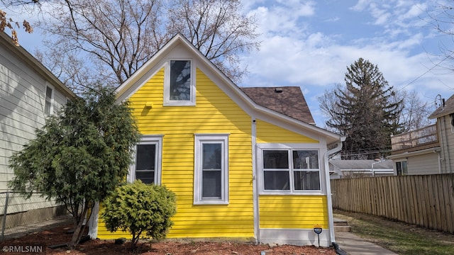 view of side of home featuring roof with shingles and fence