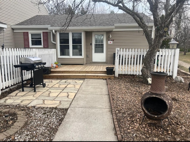 back of property with a wooden deck, roof with shingles, and fence