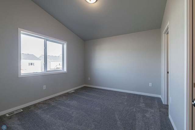 spare room featuring visible vents, baseboards, dark carpet, and lofted ceiling