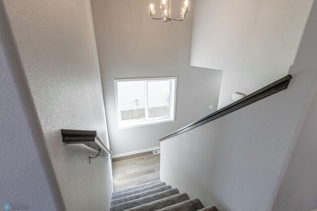 staircase with wood finished floors, an inviting chandelier, baseboards, and visible vents