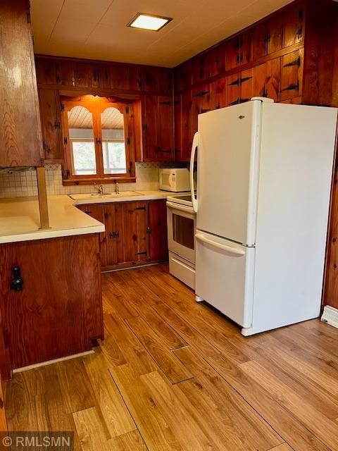 kitchen with a sink, light countertops, white appliances, and light wood-style floors