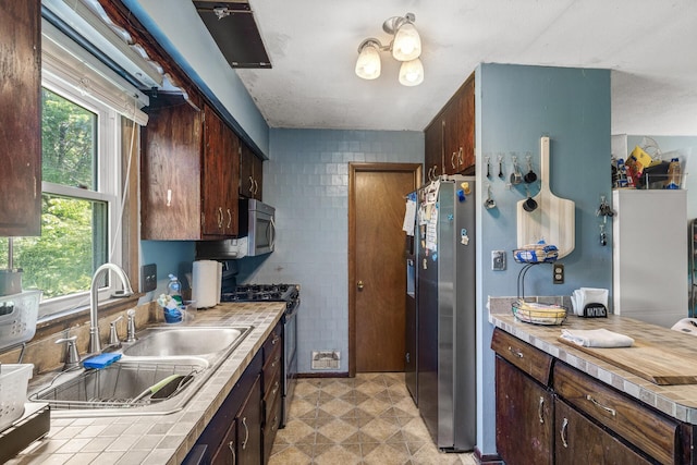 7716 Orchard Ave N, Brooklyn Park, MN 55443 - kitchen featuring stainless steel appliances, a sink, tile countertops, dark brown cabinetry, and tile walls