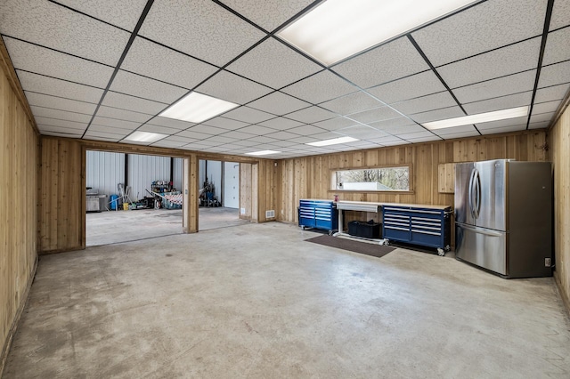 basement featuring a paneled ceiling, wood walls, and freestanding refrigerator