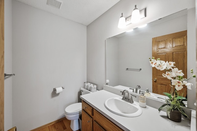 bathroom featuring vanity, toilet, visible vents, baseboards, and wood finished floors