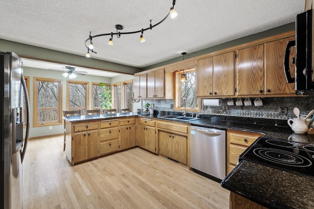 kitchen with a sink, tasteful backsplash, light wood-type flooring, black appliances, and a peninsula