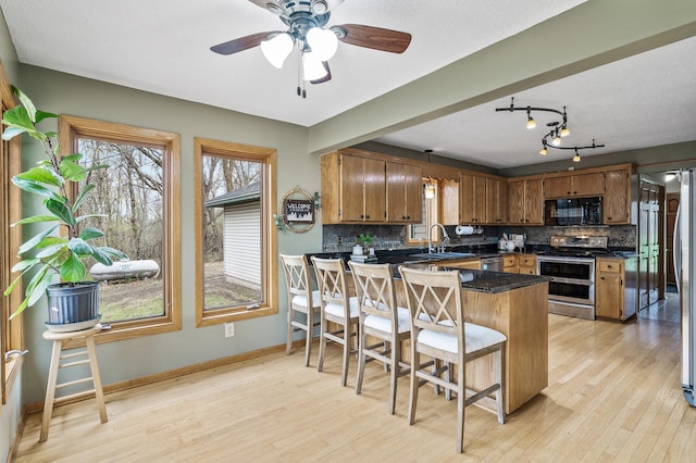 kitchen with tasteful backsplash, light wood-style flooring, appliances with stainless steel finishes, dark countertops, and a peninsula